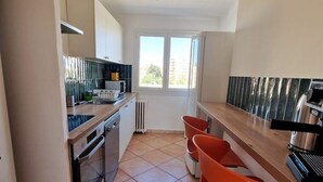 A compact kitchen with a stove, oven, and modern appliances. There is a window providing natural light and a view of the outside. - Large, modern, air-conditioned T4 (Montpellier)