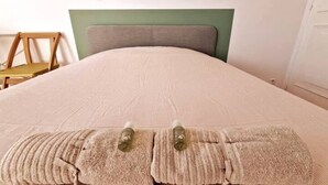 A bed with a beige cover, a green headboard, and two bottles on the bed. - Large, modern, air-conditioned T4 (Montpellier)