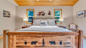 A bedroom with a wooden headboard, a bed with white bedding, two bedside lamps, and a window with a view of trees. - Modern Retreat in Truckee with A/C & Game Room (Truckee)