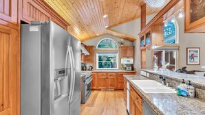 A kitchen with wooden cabinets, a stainless steel refrigerator, granite countertops, and a large window. - Modern Retreat in Truckee with A/C & Game Room (Truckee)