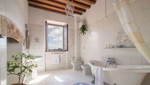 A bathroom with a bathtub, two toilets, a window, a potted plant, and a shower curtain. - Comfort two-room apartment with a view (Toscana)