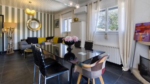 A dining area with a glass table, black and multicolored chairs, a sofa with yellow cushions, a decorative mirror, and a painting on the wall. - Gorgeous home in Royan (Royan)