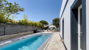 A swimming pool with lounge chairs and umbrellas, a stone wall, and a building with a modern design. - Gorgeous home in Royan (Royan)