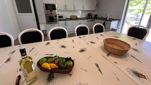 Een eethoek met een tafel gedekt voor zes personen, een fles drank en een mand met fruit.