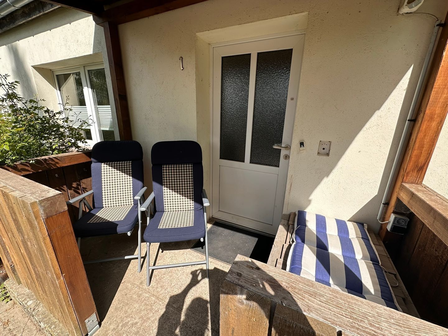 A small outdoor seating area with two chairs and a bench, a door, and a wooden deck.