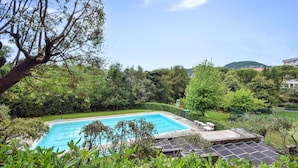 A swimming pool surrounded by lush greenery, with solar panels and outdoor furniture.