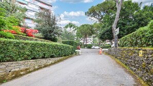 A narrow road flanked by stone walls and greenery, leading to a building with a red roof.
