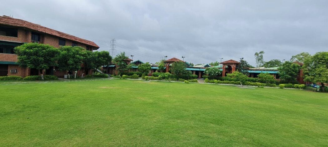A hotel with multiple buildings, a large grassy lawn, and trees.