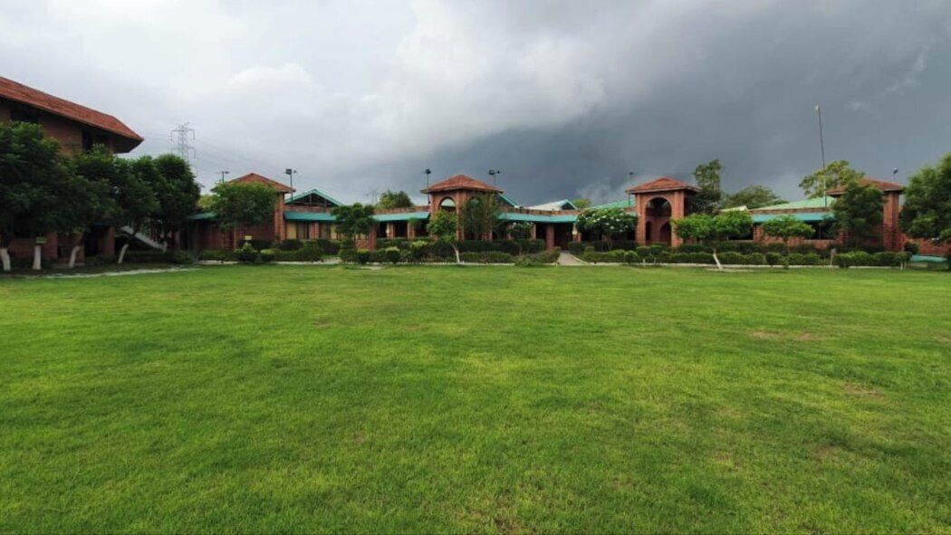 A large grassy area with a row of buildings featuring arched walkways and red roofs.