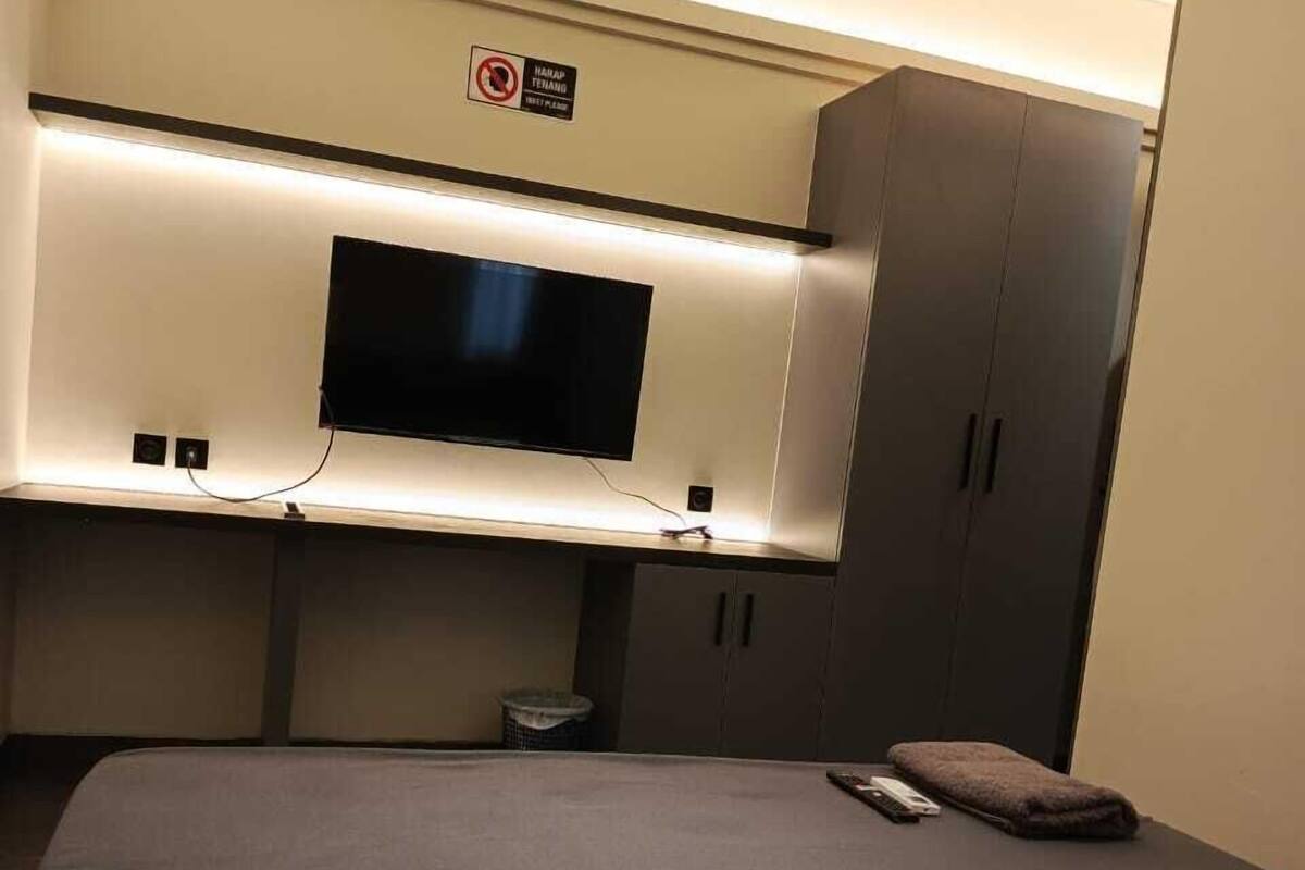 A compact hotel room with a bed, a flat-screen TV mounted on a wall, and a wardrobe.