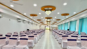 A conference room with rows of chairs covered in white and navy blue sashes, a chandelier, and a tiled floor. - Hotel Aaditya Inn Tathawade (Paud)