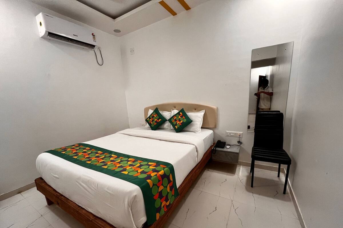 A hotel room with a bed, a bedside table with a phone, and a wall-mounted air conditioning unit.