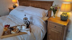 A neatly made bed with white linens, a bedside table with a lamp, and a tray with breakfast items including toast, coffee, and fruit. - Quiet, rural hideaway in traditional old Schoolhouse, right on the edge of loch. (Isle of Lewis)