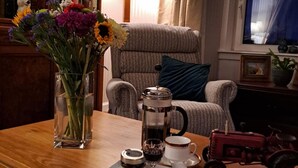 A cozy living room with a wooden coffee table, a bookshelf, a comfortable armchair, a lamp, and a window with a view. - Quiet, rural hideaway in traditional old Schoolhouse, right on the edge of loch. (Isle of Lewis)