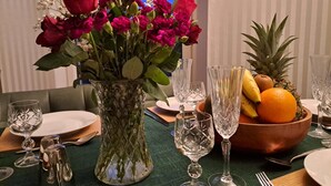 A dining table set with a vase of flowers, crystal glasses, a fruit bowl, and cutlery. - Quiet, rural hideaway in traditional old Schoolhouse, right on the edge of loch. (Isle of Lewis)