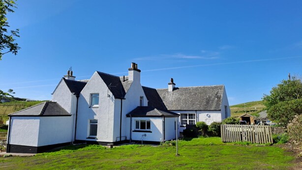 A two-story white house with a grey roof, surrounded by a grassy yard and a wooden fence. - Quiet, rural hideaway in traditional old Schoolhouse, right on the edge of loch. (Isle of Lewis)