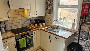 Una cocina moderna con armarios blancos, piso de madera en patrón de espiga y ventana con vistas al exterior.
