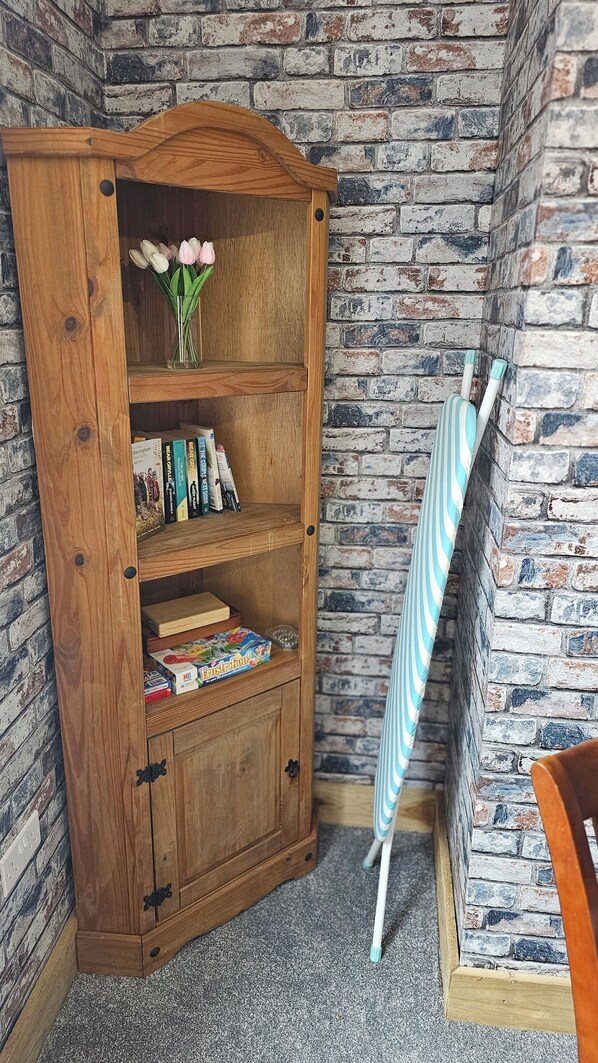 A wooden bookcase with books and a vase of flowers, against a brick wall.