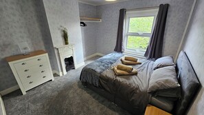 Une chambre à coucher avec un lit, une commode, une cheminée et une fenêtre avec des rideaux.