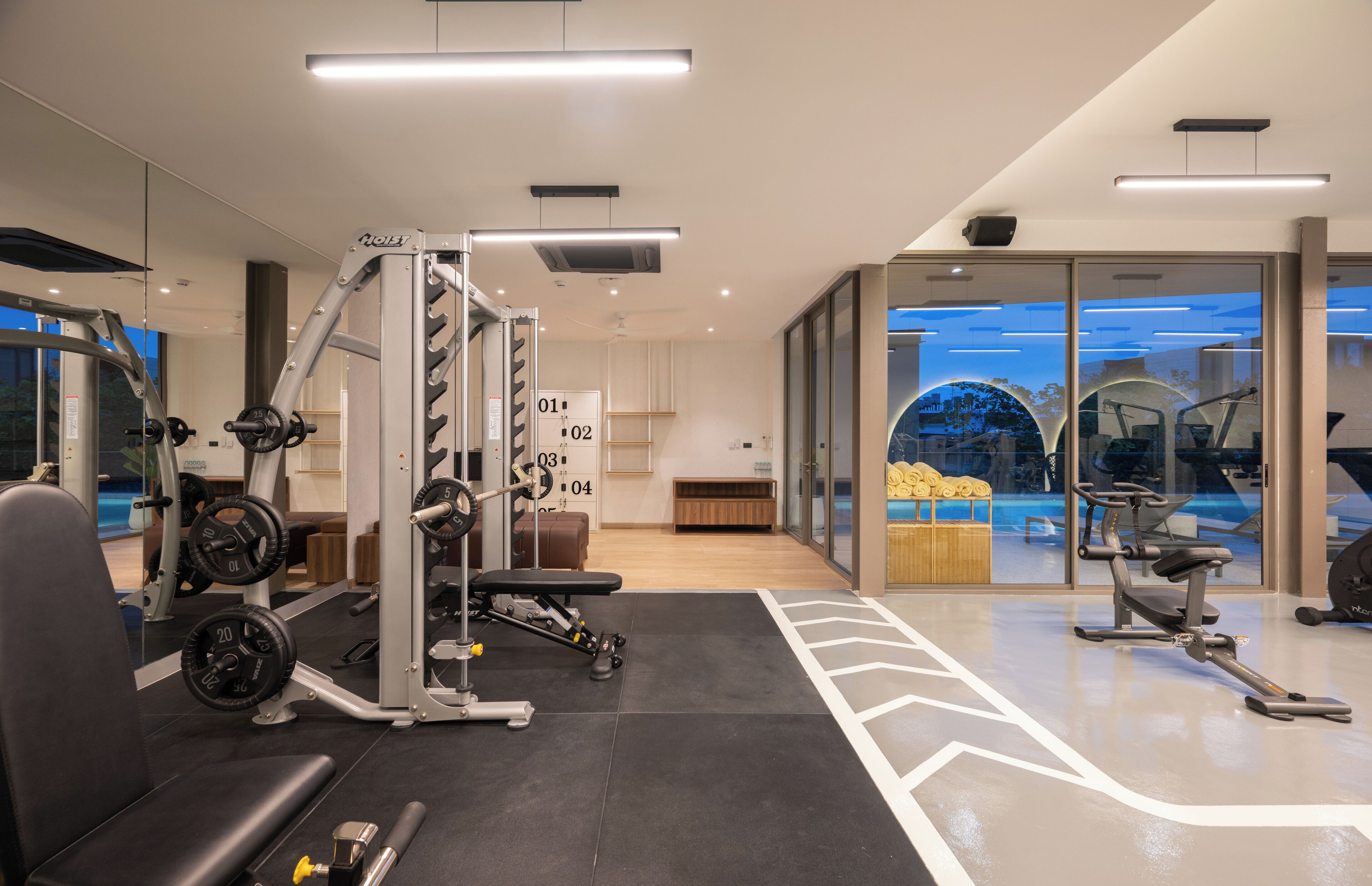 Un gimnasio moderno con máquinas de pesas, una banca y un muro espejado.