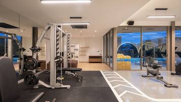 Un gimnasio moderno con máquinas de pesas, una banca y un muro espejado.
