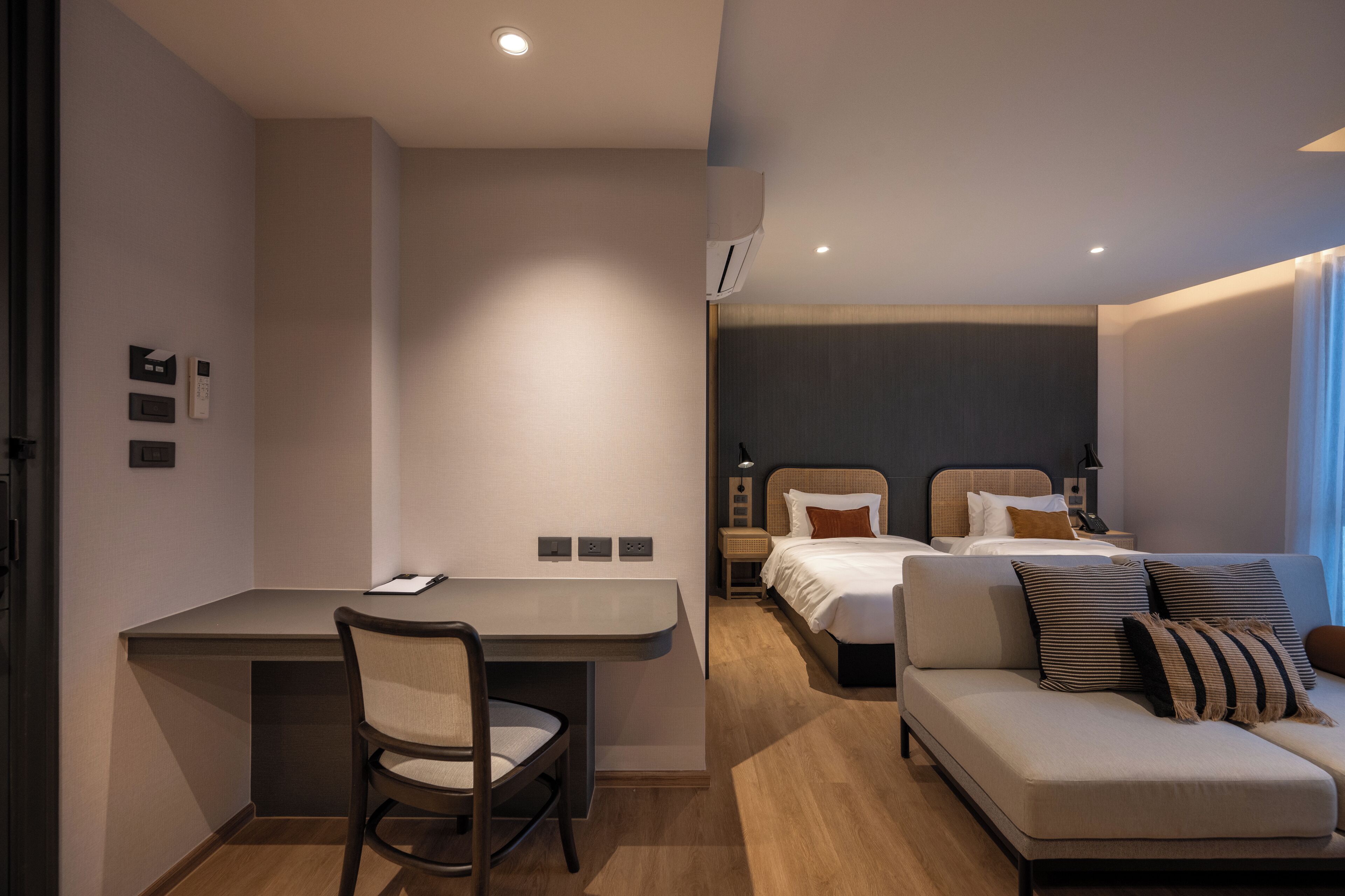 A modern hotel room with a desk, chair, bed, and sofa.