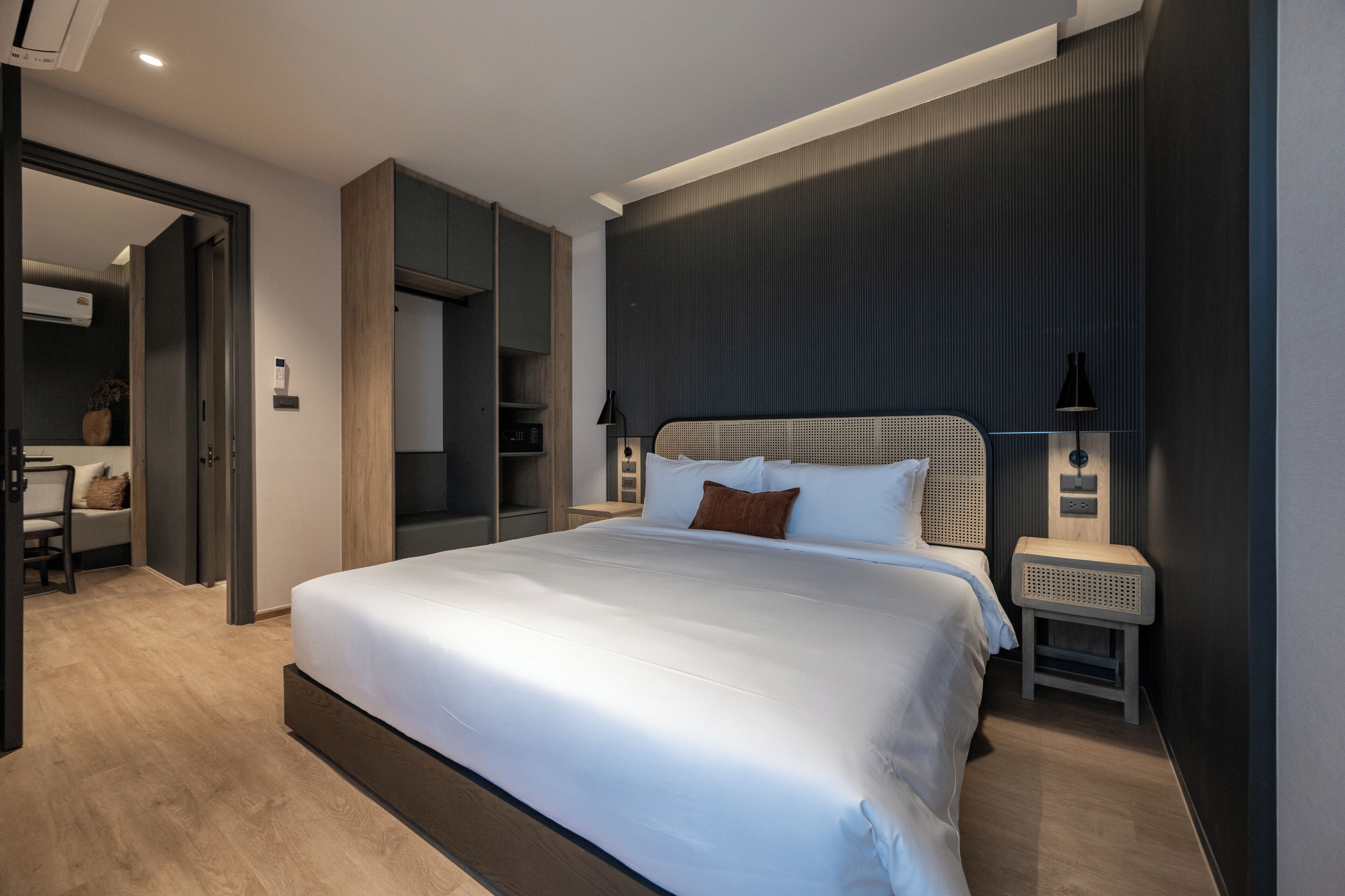 A modern bedroom with a large bed, built-in wardrobe, bedside tables, and a small seating area.