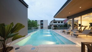 A swimming pool with lounge chairs and exercise equipment, surrounded by modern buildings and a potted plant. - The Moment (Bangkok)