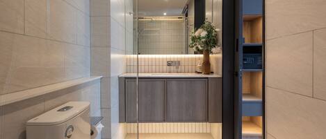 A modern bathroom with a toilet, shower, and a glass partition leading to a kitchen area.