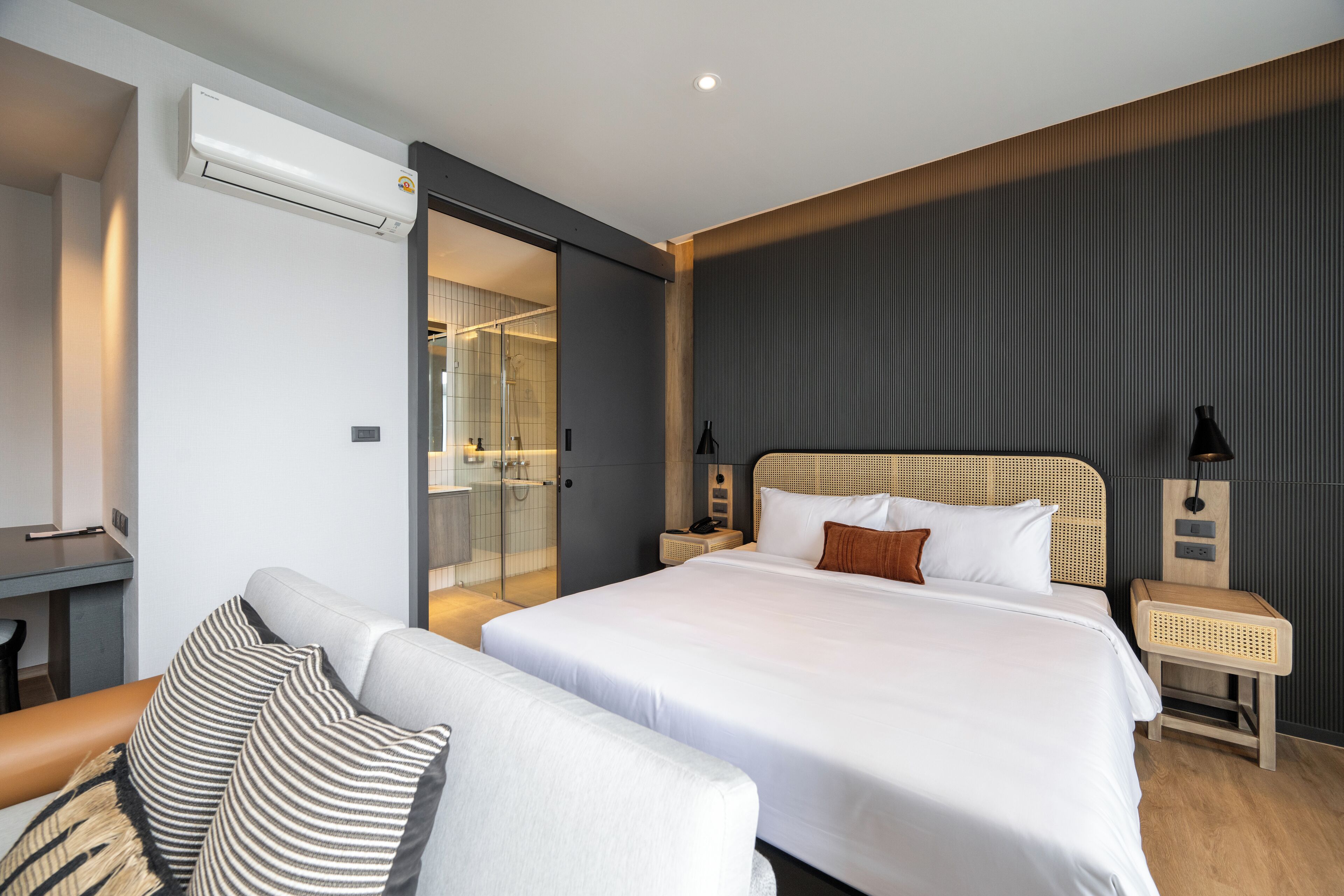 A modern hotel room with a large bed, a seating area with a sofa and armchair, a small table, and a walk-in shower.