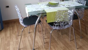 Ein Essbereich mit einem Glastisch und Stühlen, einer grünen Tischdecke und einem Gemälde einer Küstenlandschaft an der Wand.