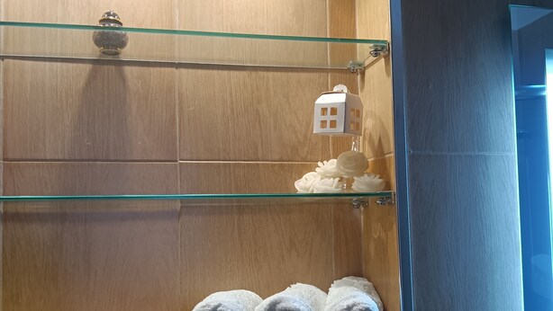 Ein Badezimmer mit Holzwänden, einer Glasablage mit einem hausförmigen Schmuckstück und aufgerollten Handtüchern.