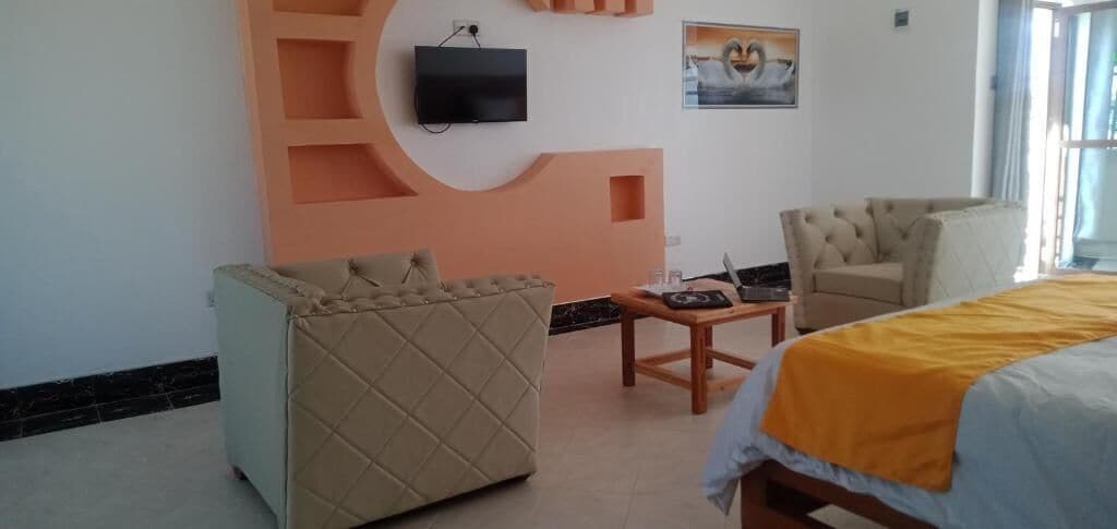 Une chambre d’hôtel avec un lit, un canapé, une chaise, une télévision et une petite table.