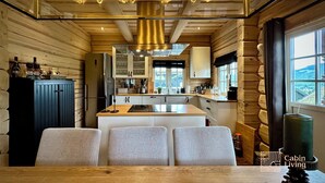 A modern kitchen with wooden walls, a central island, and pendant lighting. - Stylish log cabin in Hafjell w/view & sauna (Øyer kommune)