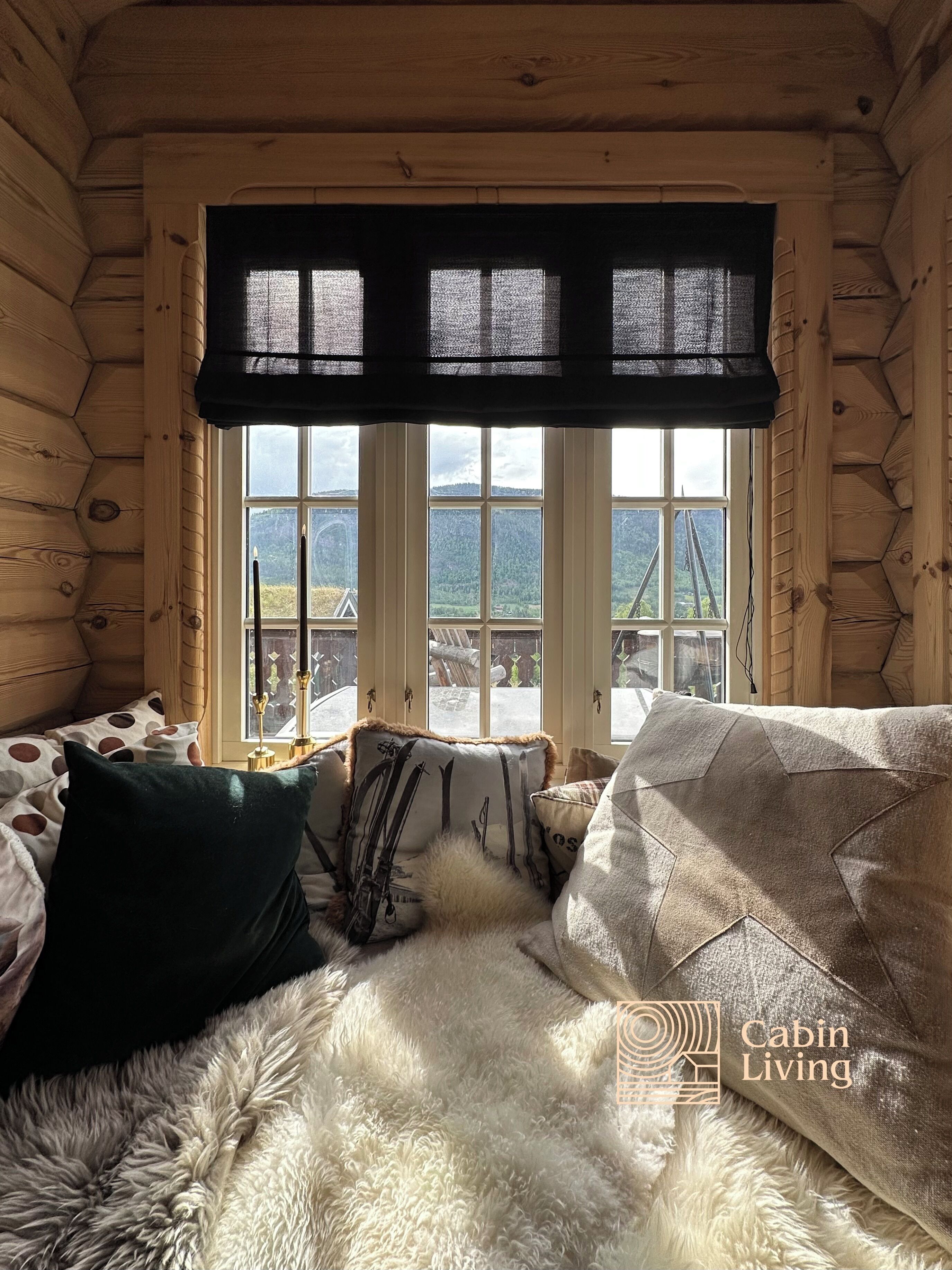 Ein Holzhäuschen-Interieur mit großem Fenster, einem Fellteppich und einem Bett mit Kissen in Punkte- und Vollfarben.
