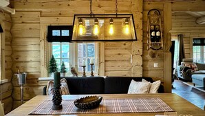 A cozy cabin interior with a wooden log wall, a dining table with chairs, a hanging light fixture, and a small Christmas tree. - Stylish log cabin in Hafjell w/view & sauna (Øyer kommune)