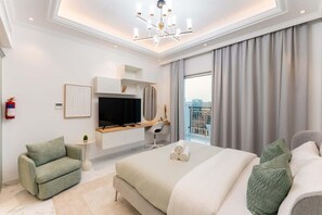 A modern hotel room with a large bed, a desk with a flat-screen TV, a sofa, and a view of the city.