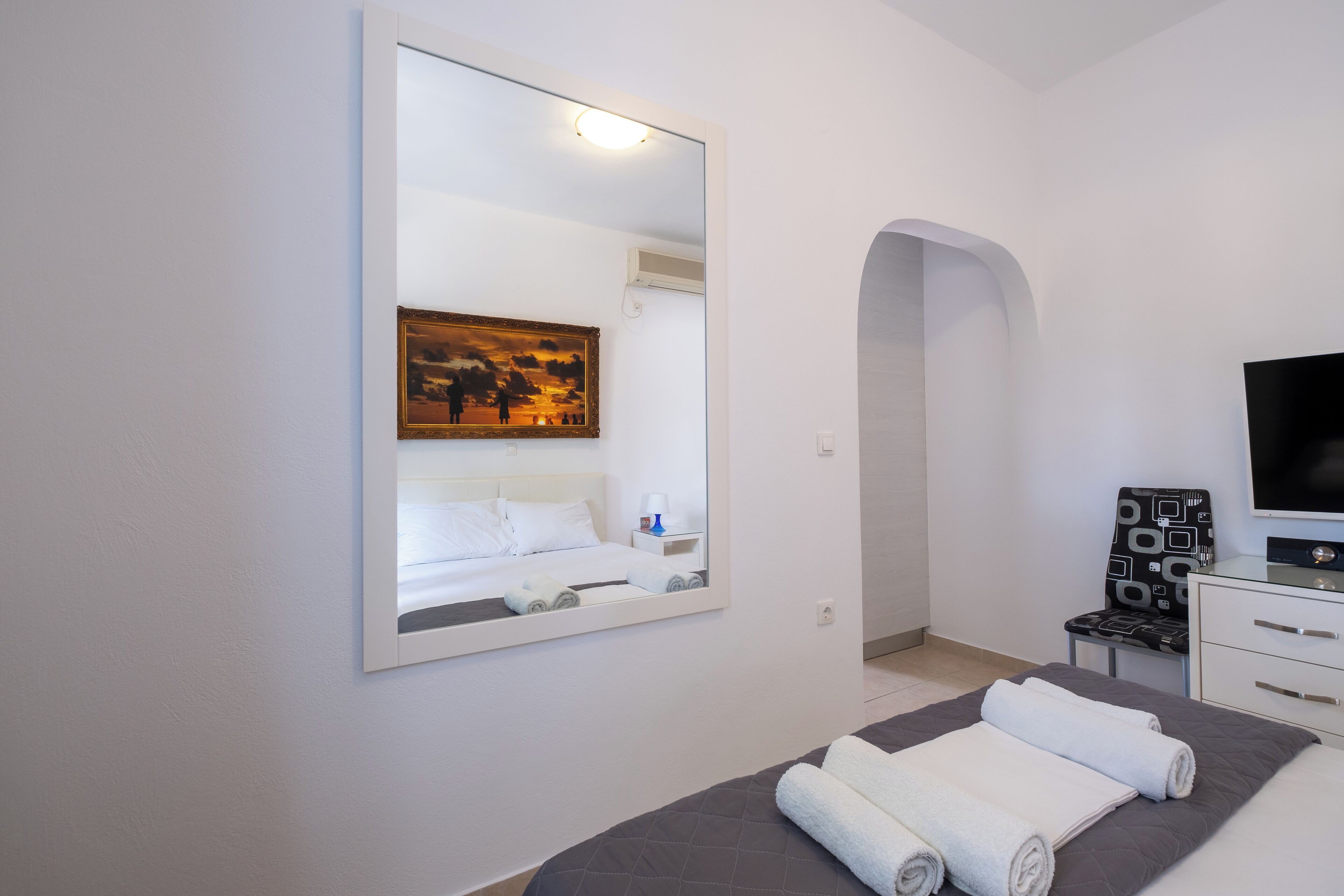 A modern hotel room with a large bed, a flat-screen TV, a painting above the bed, and a small desk with a chair.