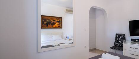 A modern hotel room with a large bed, a flat-screen TV, a painting above the bed, and a small desk with a chair.