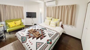 Una habitación de hotel con una cama, un sofá verde, un televisor y un equipo de aire acondicionado.