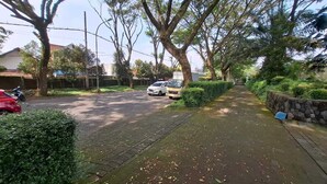 A residential street with a paved sidewalk, parked cars, and trees.