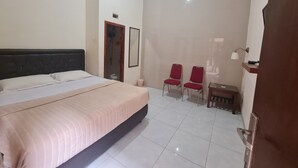 A hotel room with a bed, two red chairs, a small table, a mirror, and a door leading to a bathroom.
