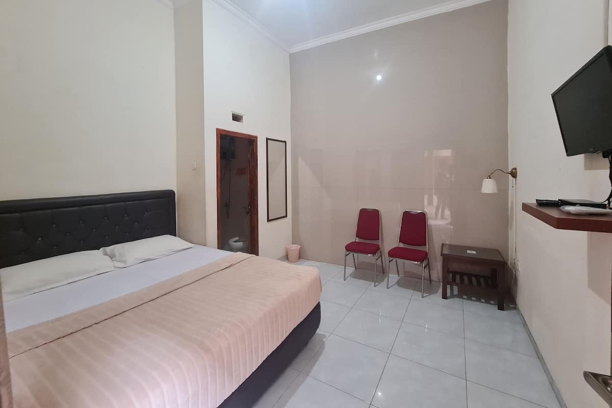 A bedroom with a bed, two red chairs, a desk, a television, and a small bathroom.