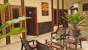 A lobby with a glass-top table, wooden chairs, and large green plants.