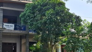 A building with a sign reading "TERIMA KOST" and a large tree in front.