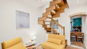 A modern living room with a wooden staircase, a yellow sofa, and a dining area with a blue wall and a ship model.