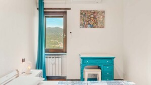 A bedroom with a bed, a nightstand, a dresser, a window with curtains, and a wall art piece.