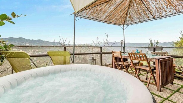 A hot tub area with a table and chairs, overlooking a scenic view of mountains and a body of water.