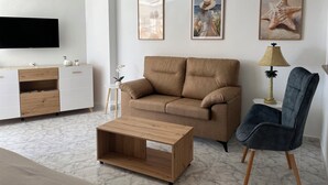 Een moderne woonkamer met een beige bank, een houten salontafel, een blauwe fauteuil, een vloerlamp en een plafondventilator.
