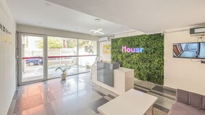 A modern reception area with a green wall, a reception desk, and a flat-screen TV. - Housr 1 RK Sector 27 Gurgaon Golf Course (Gurugram)
